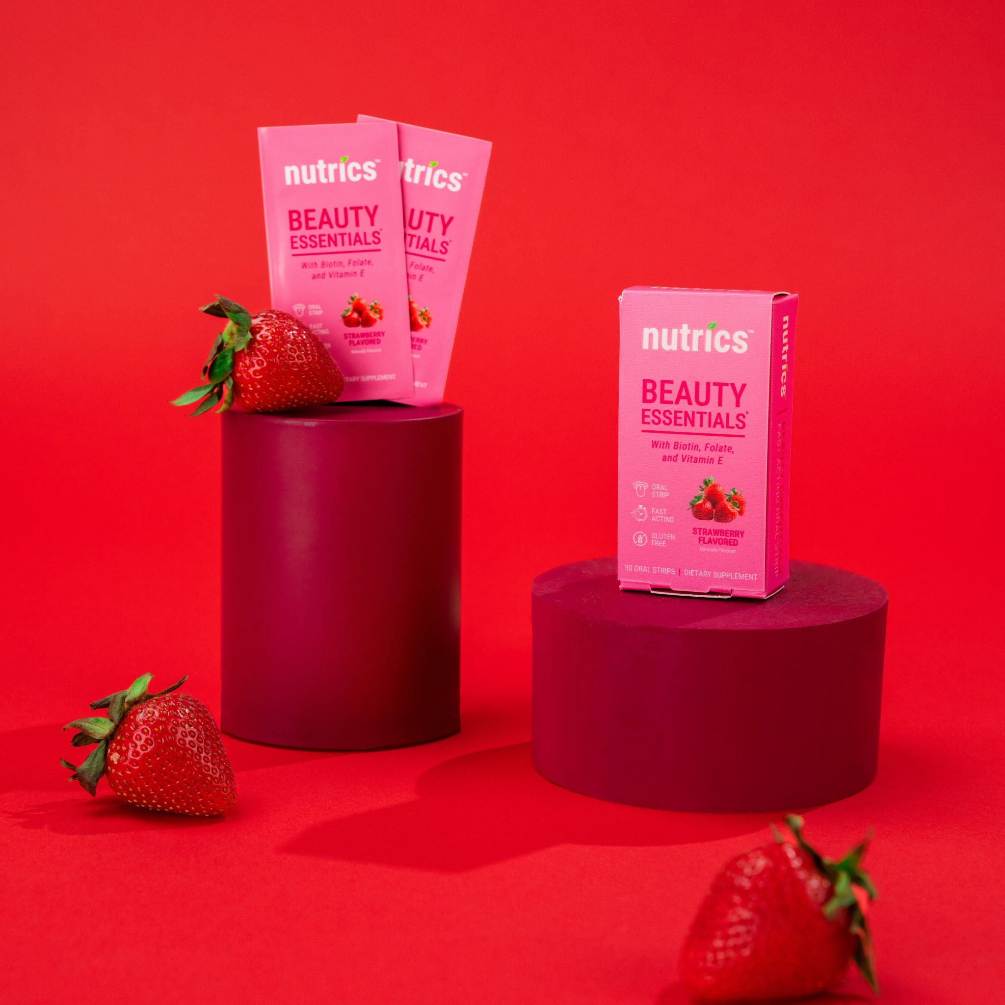Pink Nutrics beauty essential boxes on a red background with strawberries.