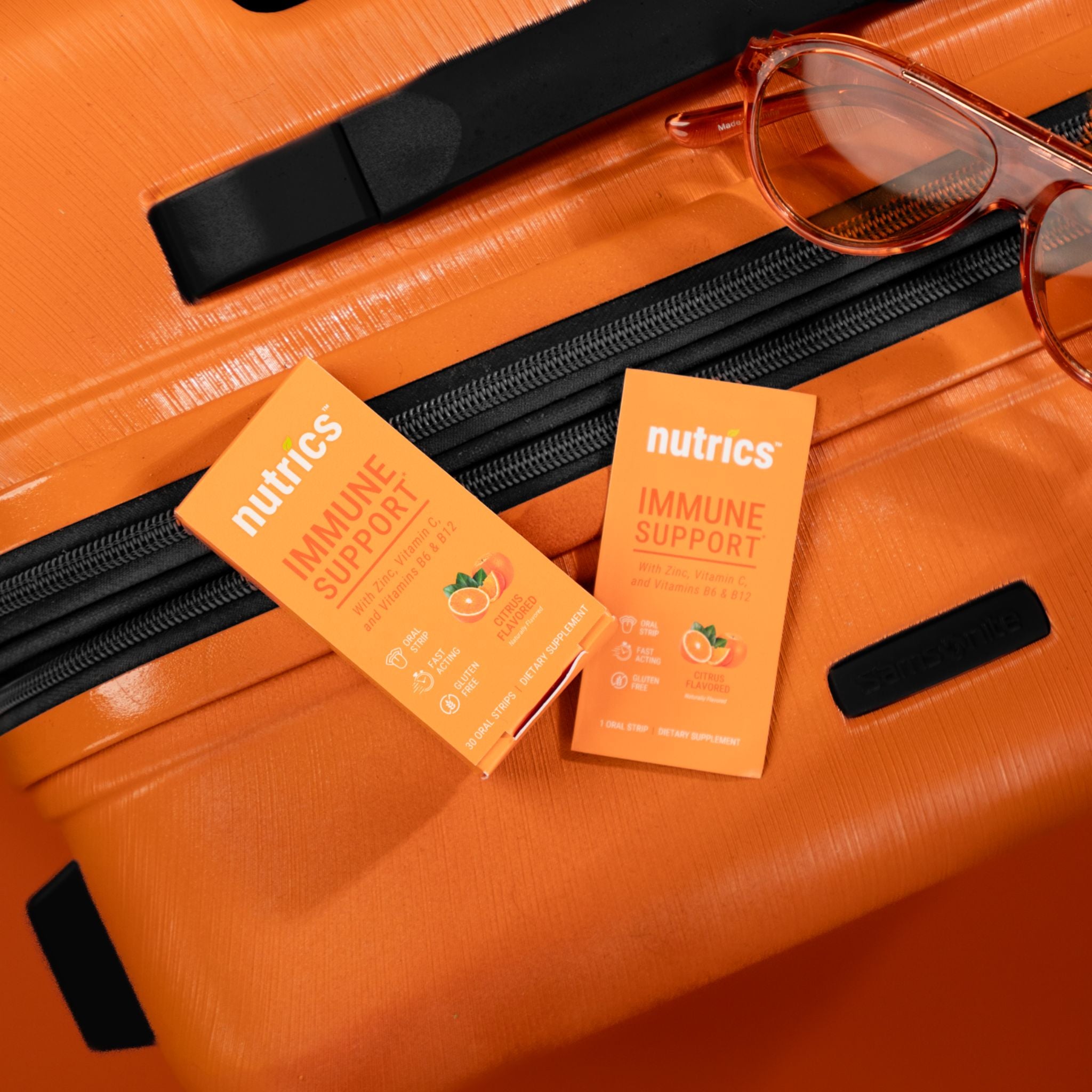 Orange suitcase with sunglasses and Nutrics Immune Support packets on top