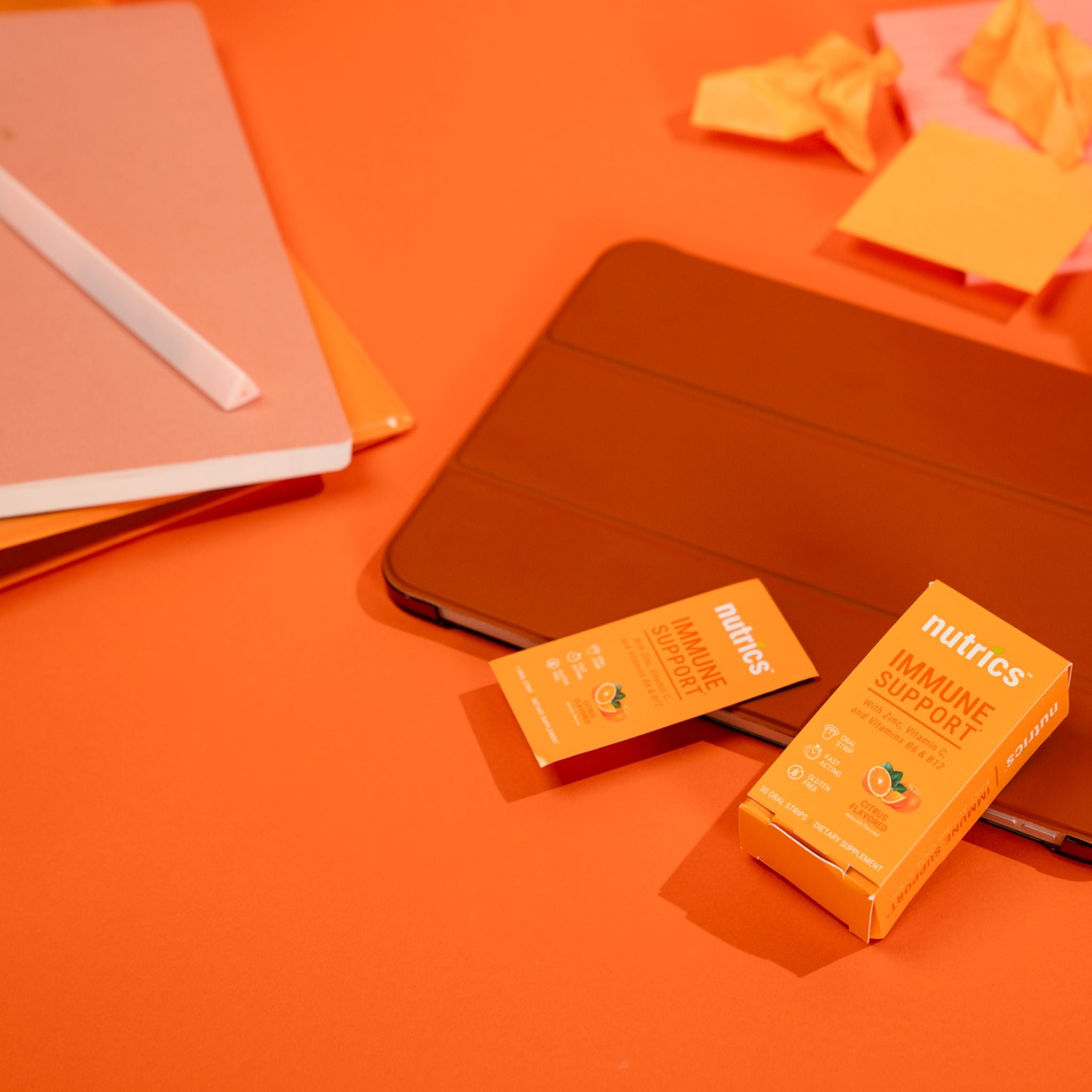  Nutrics immune support packaging on an orange background with notebooks.