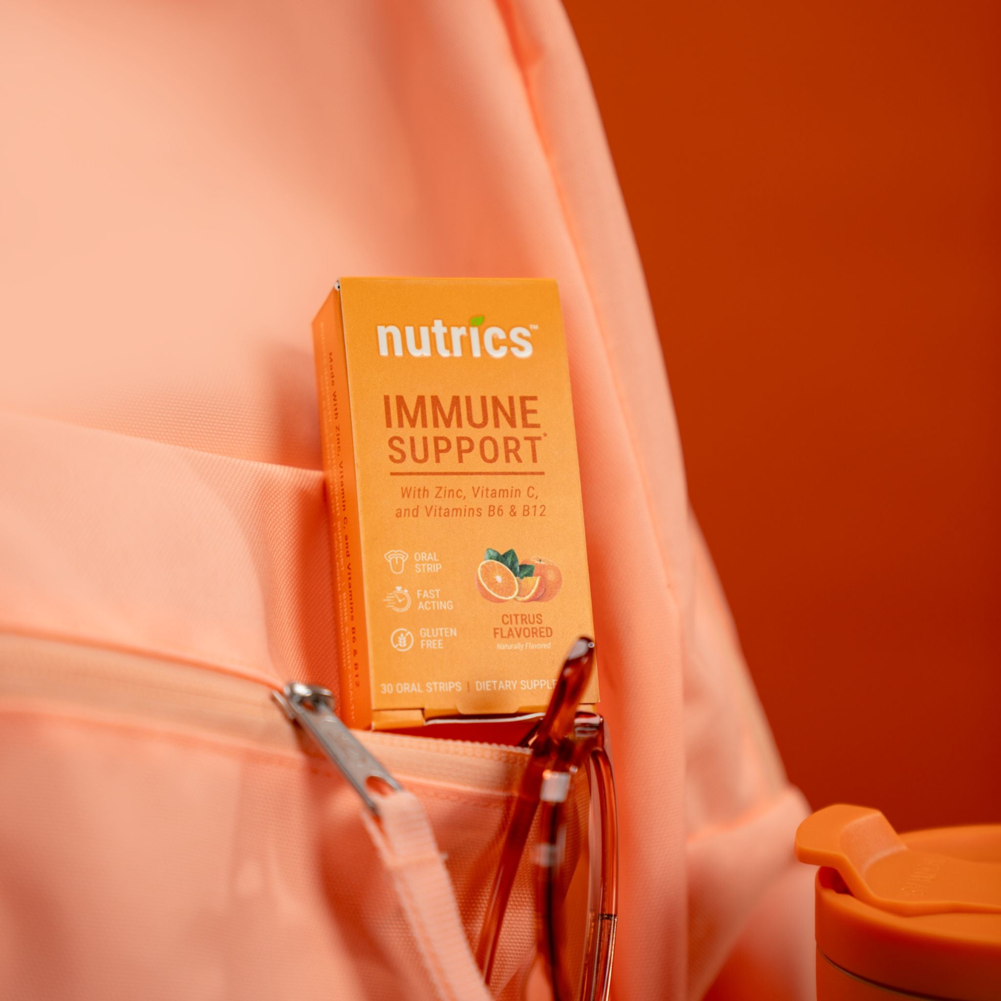 Nutrics immune support supplement box held by a person against an orange background