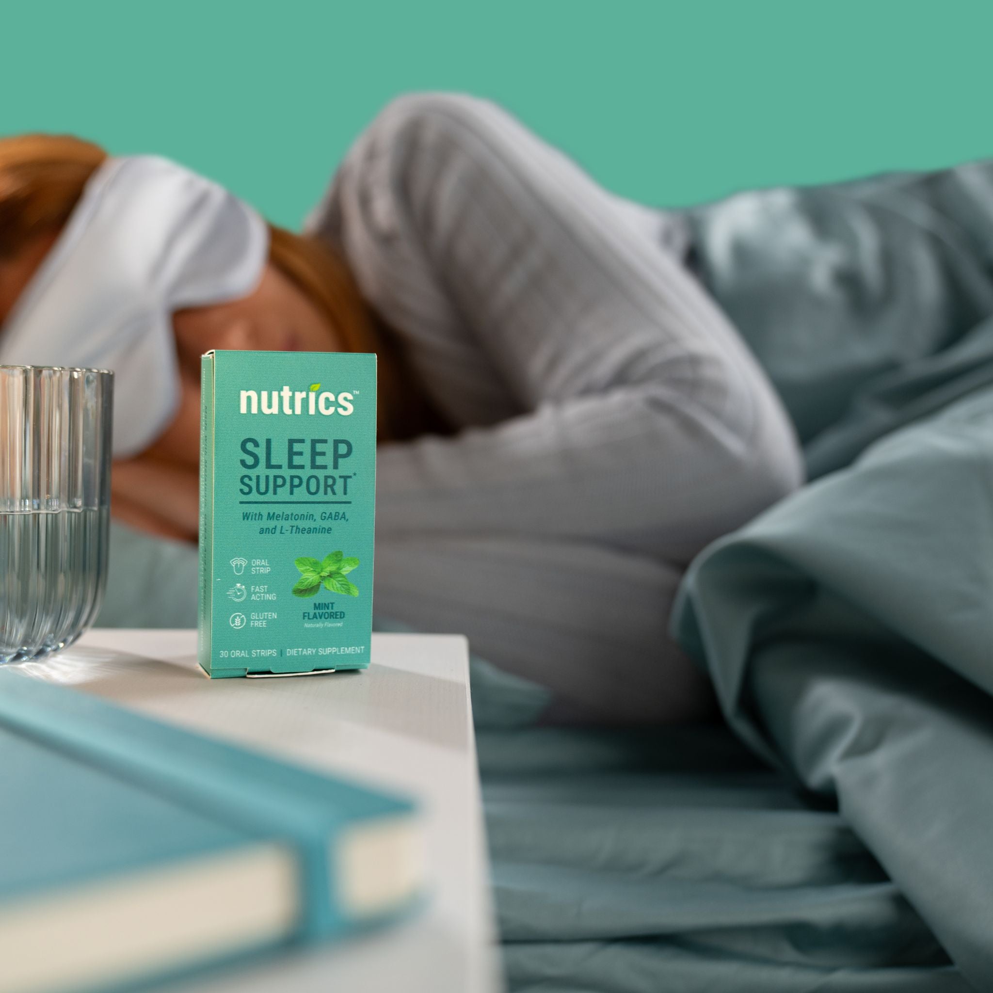 Box of Nutrics Sleep Support on a nightstand next to a person lying in bed.