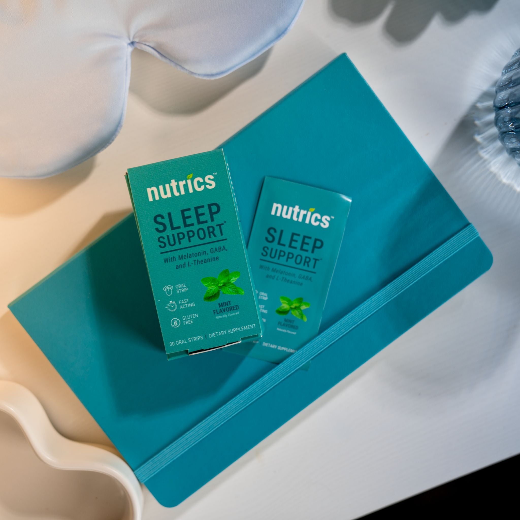 Two boxes of Nutrics Sleep Support on a teal tray with a white pillow in the background.