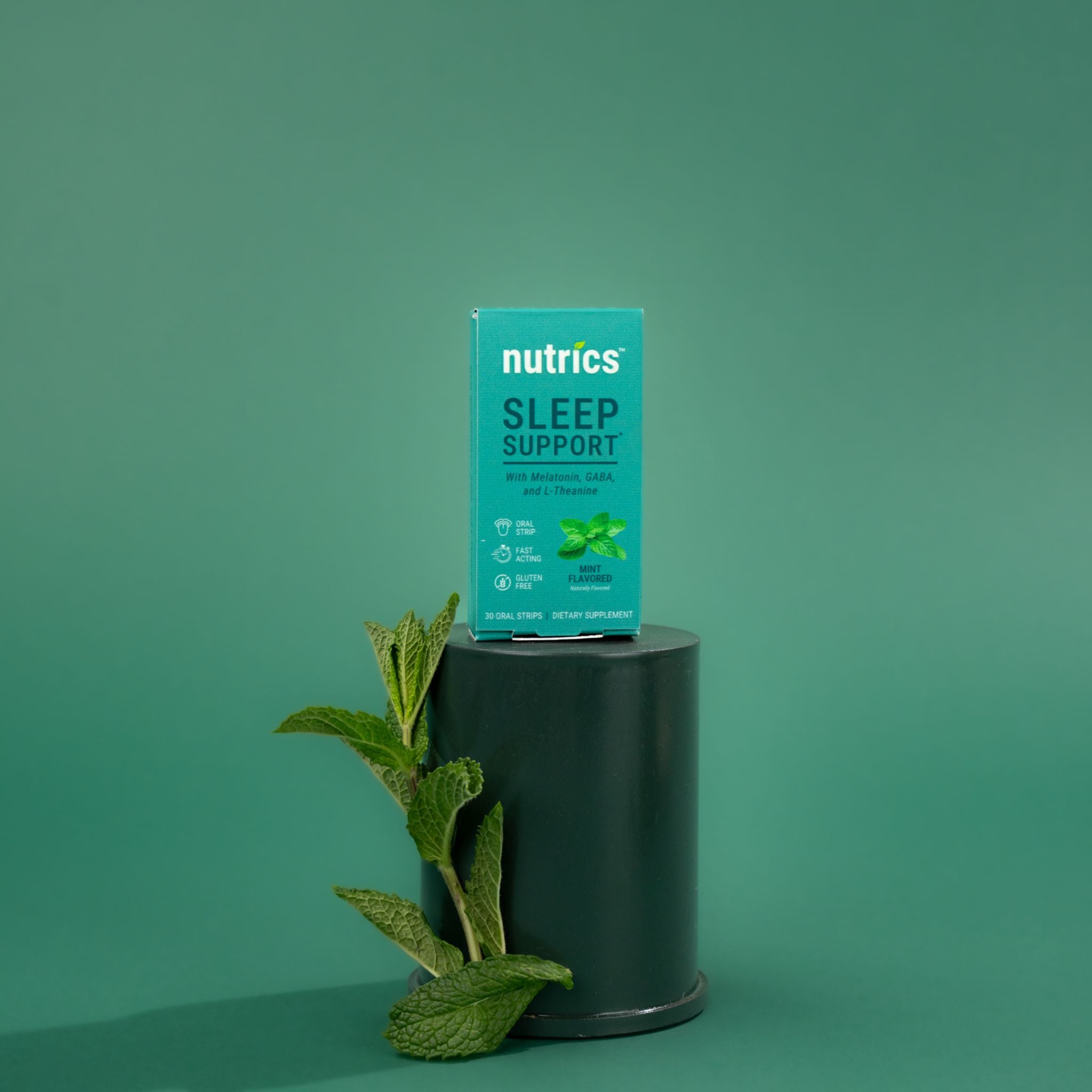 Nutrics Sleep Support packaging on a dark pedestal with mint leaves against a green background